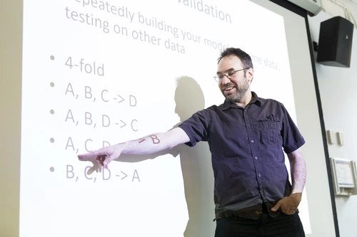 Dr. Ryan Baker points to equations on a presentation slide