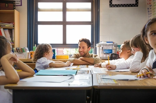 Teacher leaning on desk to be eye-level with elementary age child.