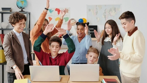 Middle-school age students cheering on two classmates sitting behind two computers
