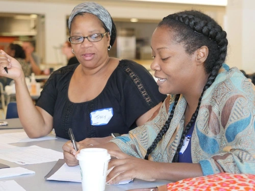 two women engage in conversation with each other while one writes on a piece of paper
