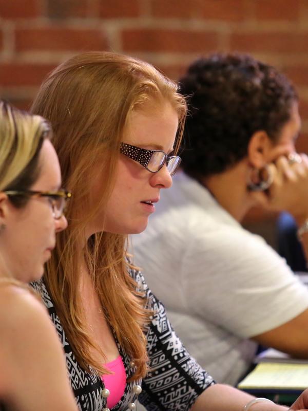 Female graduate students sitting at table, looking at laptops and talking.