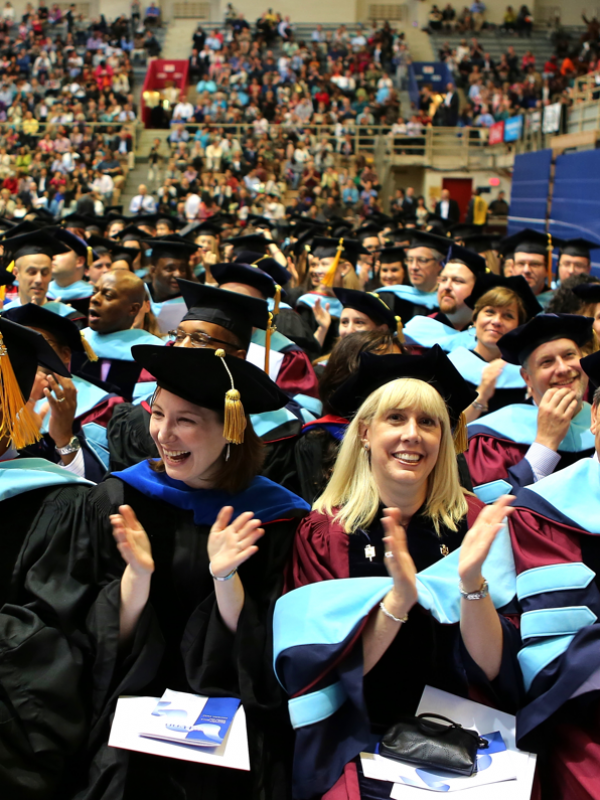 Graduate students in caps and gowns sitting and clapping 