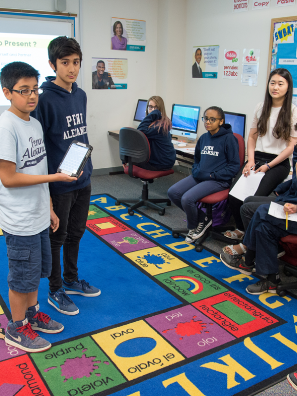 Middle school students with tablet standing at front of class