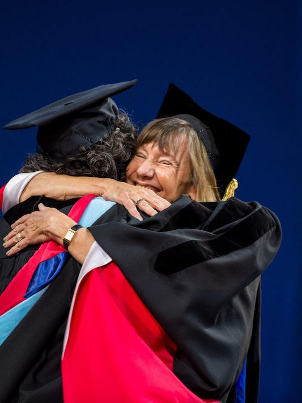 Dean Grossman and a student embrace onstage at graduation.