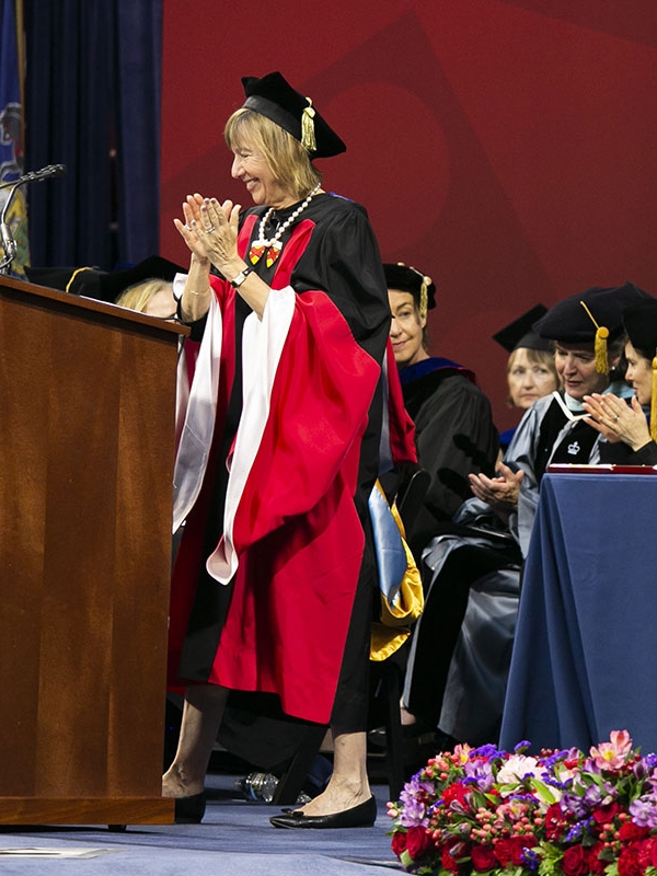 Penn GSE’s dean and faculty are onstage wearing graduation caps and gowns, applauding with smiles on their faces during a commencement ceremony.