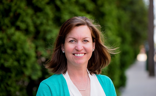 Woman in blue sweater standing outside and smiling.