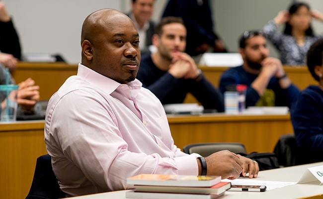 Male graduate student sitting and listening in classroom.