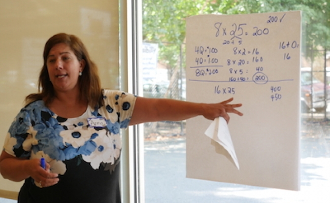 A teacher in the Responsive Math Teaching program points to a poster where she has written out solutions to a multiplication math problem.