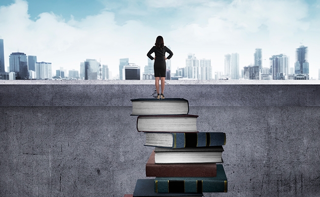 Woman standing on pile of books, looking out at a city skyline. 