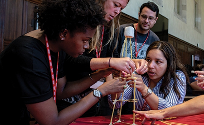 A group of teachers builds a tower from dry spaghetti on a tabletop