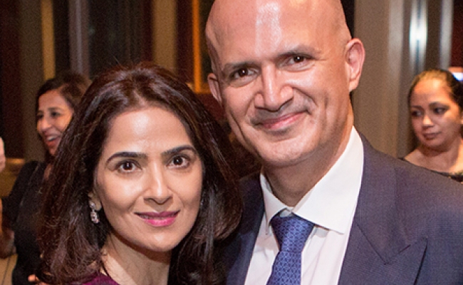 A woman in a pink blouse and a man in a suit and tie smiling while standing indoors