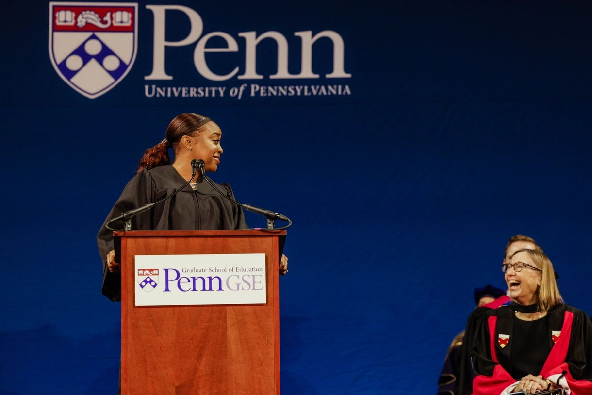 Abbott Elementary creator Quinta Brunson stands at a podium sharing a laugh with Penn GSE Dean Pam Grossman, seated to her right.