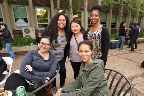 Five students sitting and standing together in a courtyard