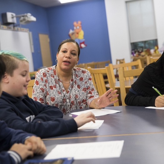A teacher and students sit around a table, before COVID-19.