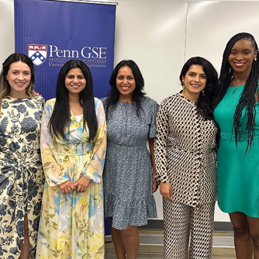 Five members of the inaugural cohort of Jacobs Fellows stand, smiling, in a classroom in front of a Penn GSE banner.