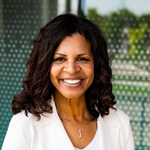 Dr. Cheryl Logan in a white suit smiles warmly, standing before a glass front building