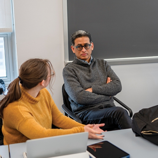 Rand Quinn sits at a table with his arms crossed engaged in discussion with two students