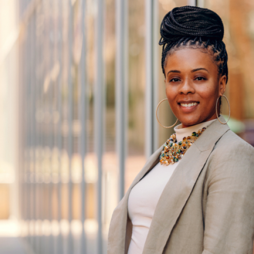 Assistant Professor Ericka Weathers pictured outside Penn GSE on a sunny spring afternoon. She is leaning against a reflective glass wall as she smiles at the camera.