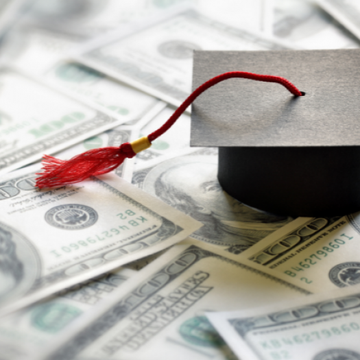 A photo illustration of a mini mortarboard (graduation cap) sitting on top a stack of $100 bills