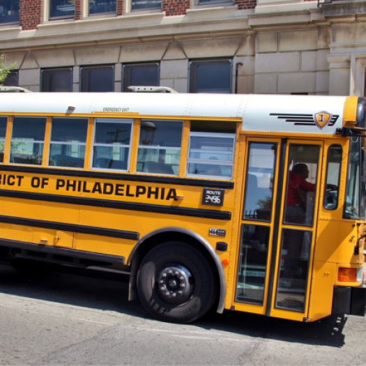 A yellow School District of Philadelphia school bus parked in front of a school.