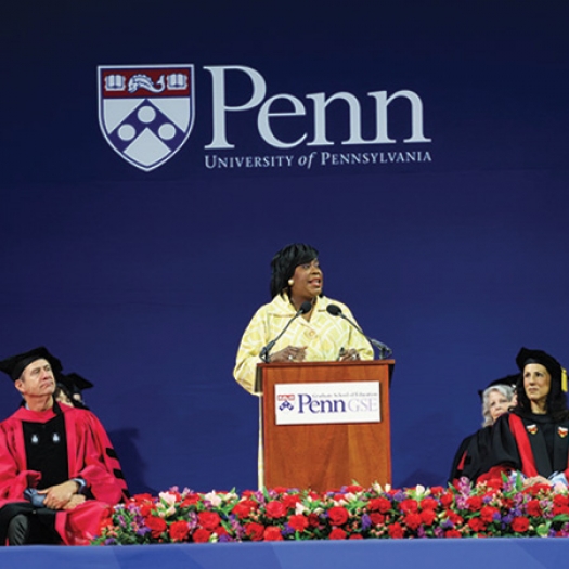 Mayor Cherelle Parker speaks at a podium while Dean Katharine O. Strunk and other faculty in regalia look on at Penn GSE's 2024 commencement ceremony