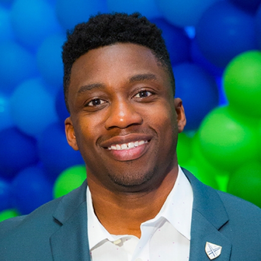 Headshot of a smiling man in a blazer in front of a background of balloons