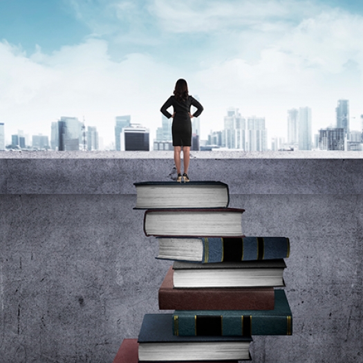 Woman standing on pile of books, looking out at a city skyline. 