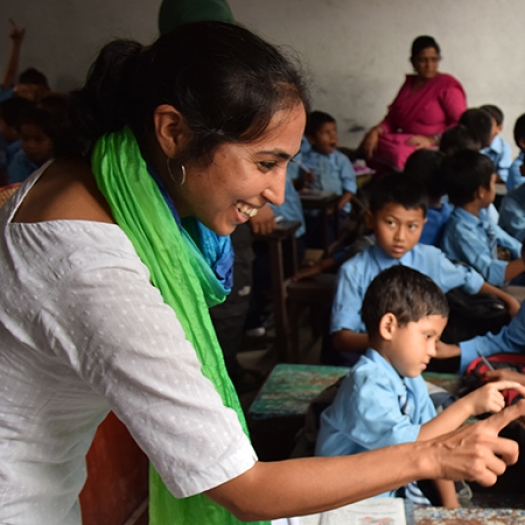 A smiling woman interacting with a class of Nepalese students 