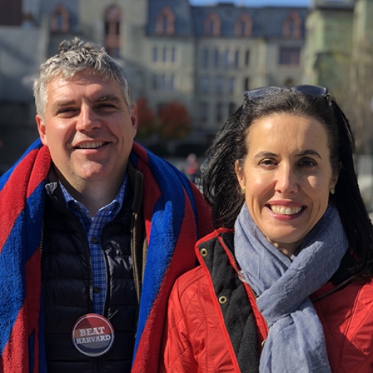 A smiling man and a woman, both in red winter coats, stand outside.