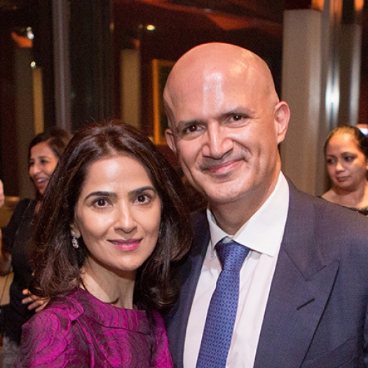 A woman in a pink blouse and a man in a suit and tie smiling while standing indoors