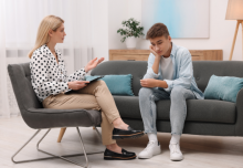 A school counselor sits in her office and talks with a mentally distressed student holding is head in his hand