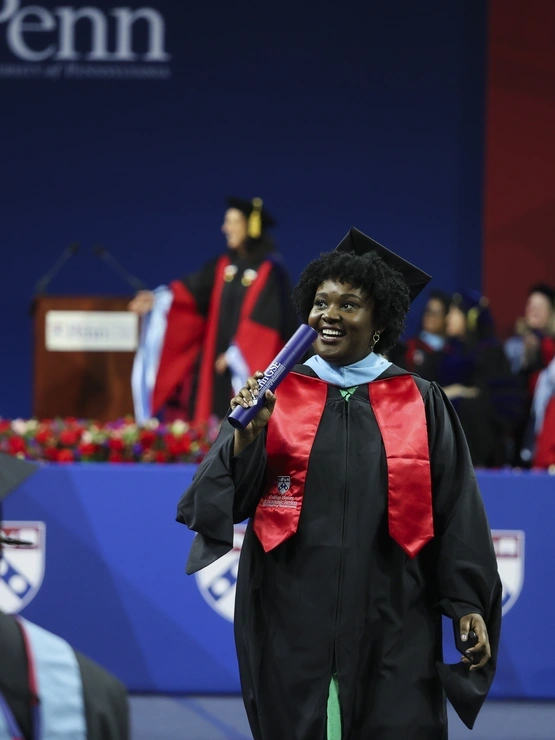 A smiling graduate in a cap and gown holds her diploma as she walks off the stage