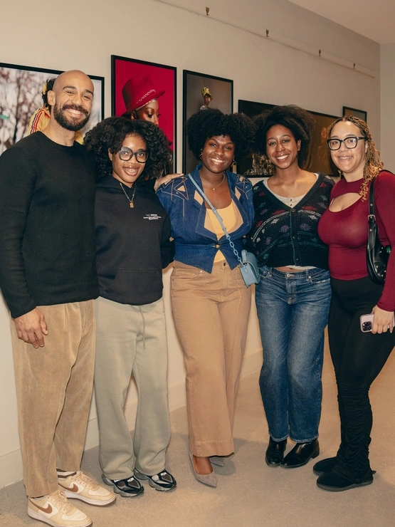 a group of people smile at the camera inside a gallery with artwork behind them on the walls