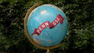 A globe with a Penn GSE ribbon painted on it in front of a shrub.