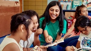 Penn GSE alum Rina Madhani sits cross-legged on the floor surrounded by elementary schoolchildren, all reading books and laughing together.