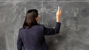 A teacher writing algebra equations on a blackboard in chalk