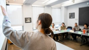 A GSE student points to her lesson on the board and she instructs a small classroom of adult learners who are seated around a table. 