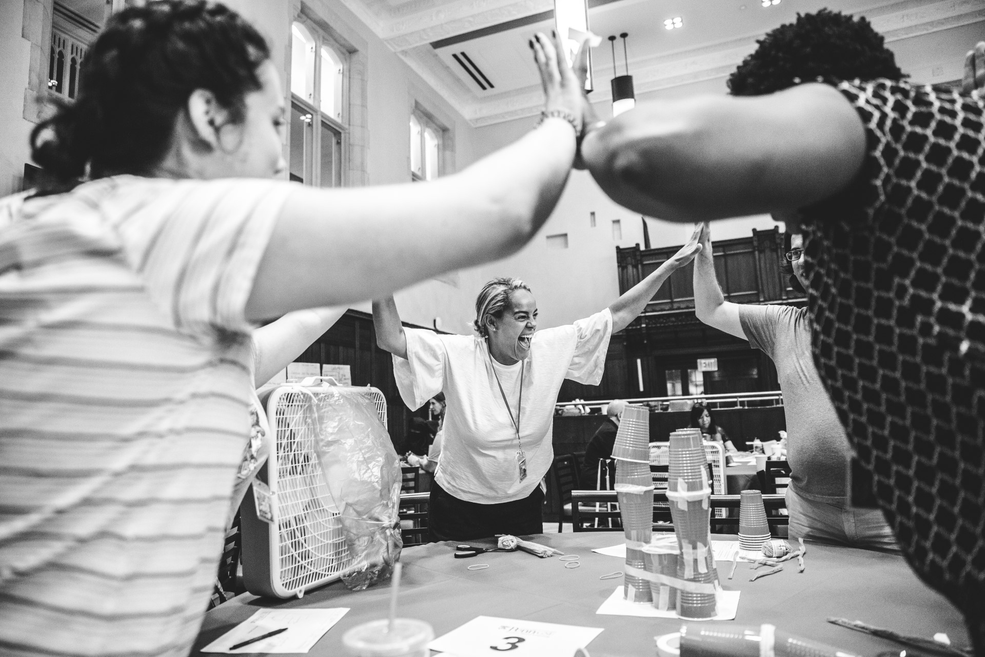 Black and white photo of people high-fiving around a table of stacked cups