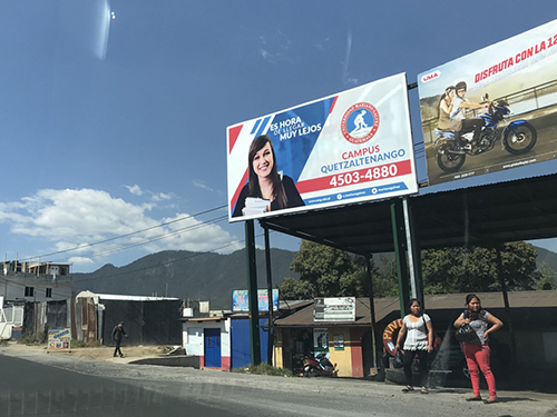 Women waiting for the bus below an ad for a private university.