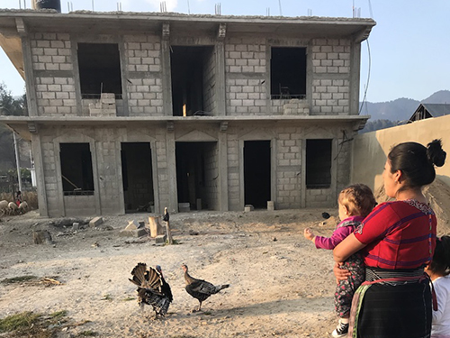 Woman holding a child looking at a two-story home under construction.