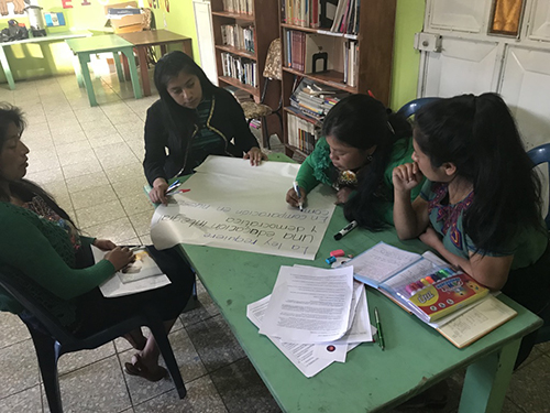 Women sitting around a table in a classroom environment investigating documents.