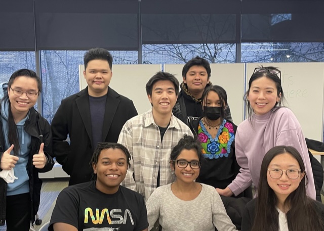 Nine teenage members of the CARE Initiative sitting and standing together in a classroom, smiling.