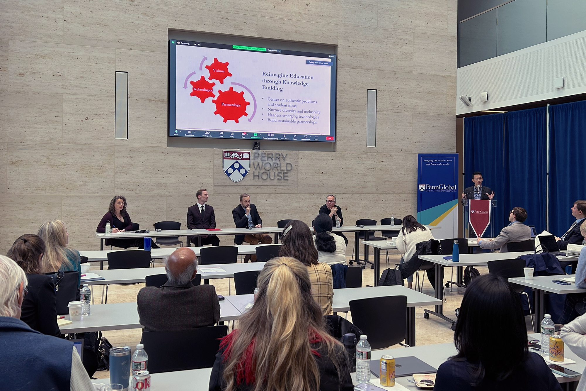 A panel sits at at table in Perry World House as a presenter on the right stands at a podium explaining his research.