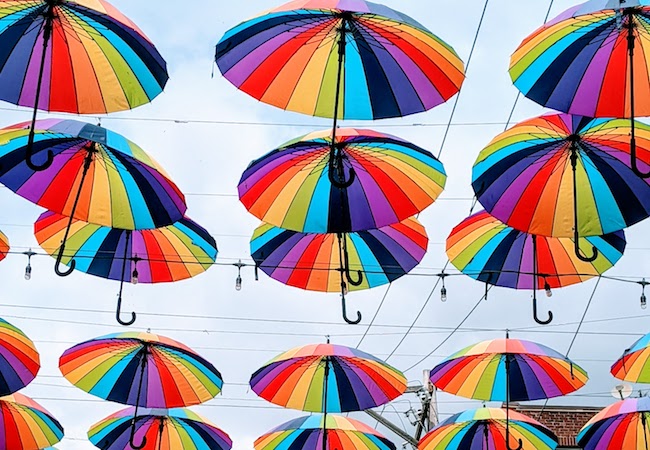 Opened rainbow patterned umbrellas displayed hanging over a street. 