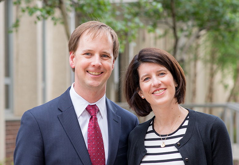 Man in suit, woman in striped top standing outside.