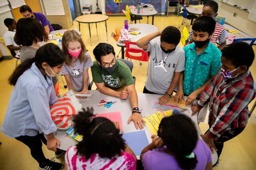 Seven students in 5th-6th grade surround their teacher as they share ideas about a math task.