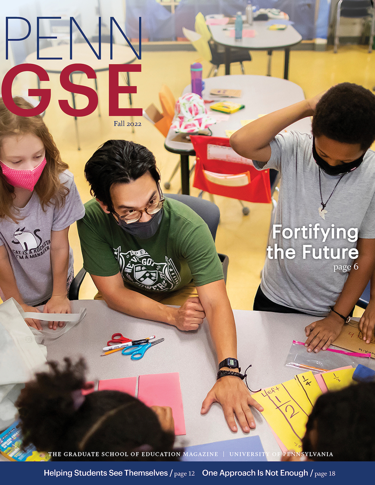 The cover of the Fall 2022 issue of The Penn GSE Magazine. A seated teacher, wearing a face mask and glasses, is surrounded by several masked elementary students and reaches across a table to engage with a student's paper. The headline reads 'Fortifying the Future.'