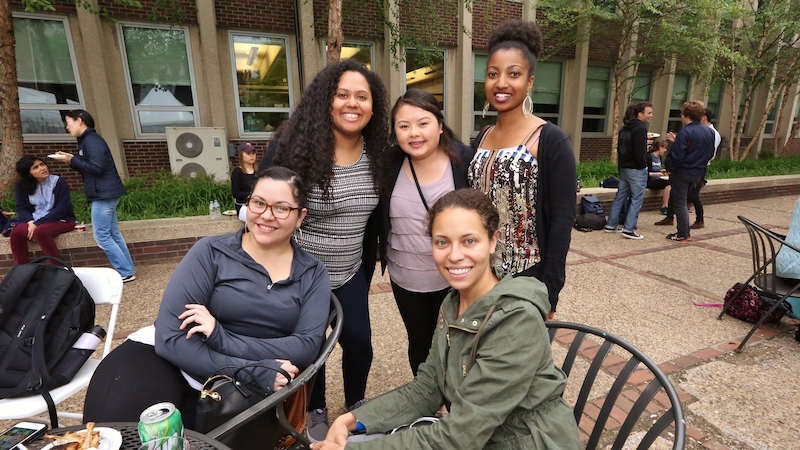 5 students sit or stand around a patio table in chilly spring weather