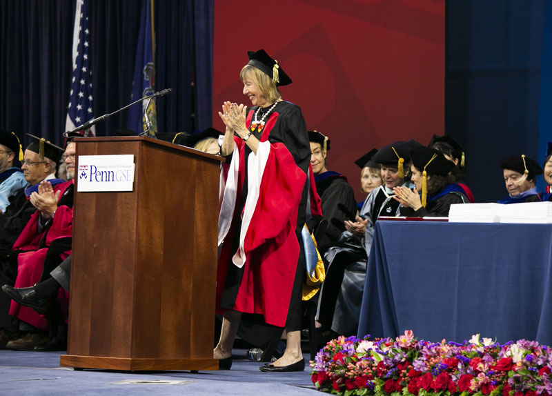 Penn GSE’s dean and faculty are onstage wearing graduation caps and gowns, applauding with smiles on their faces during a commencement ceremony.