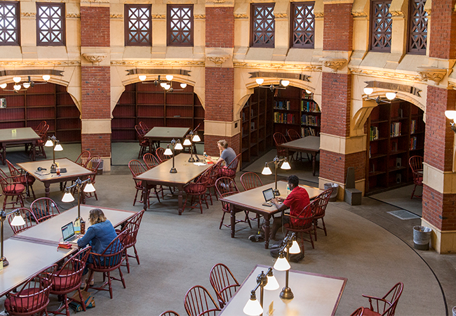 Aerial shot of three people sitting at separate tables in a library, working on laptops